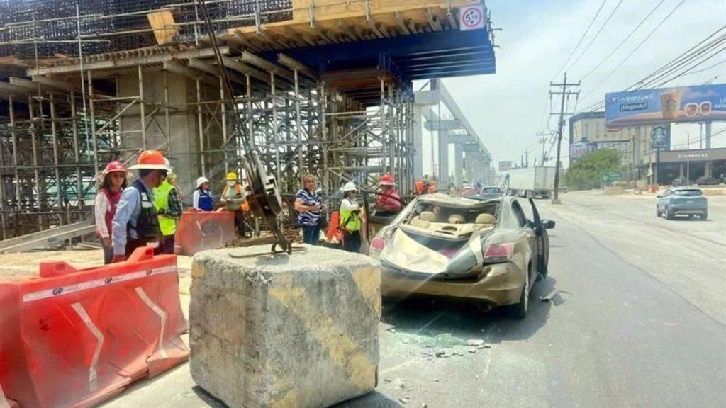 Construction workers in hard hats inspect a beige sedan that crashed into a large concrete block at a roadwork site with scaffolding nearby.