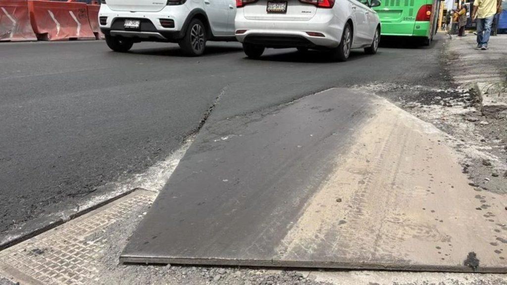 Metal ramp plate covering a curb and bridging a gap on a city street, with cars and a green bus in the background.