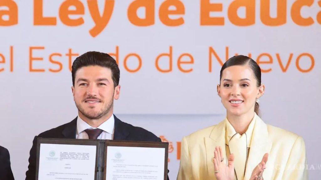 Two professionally dressed individuals pose with an opened document folder during a signing ceremony, orange banner backdrop behind them.
