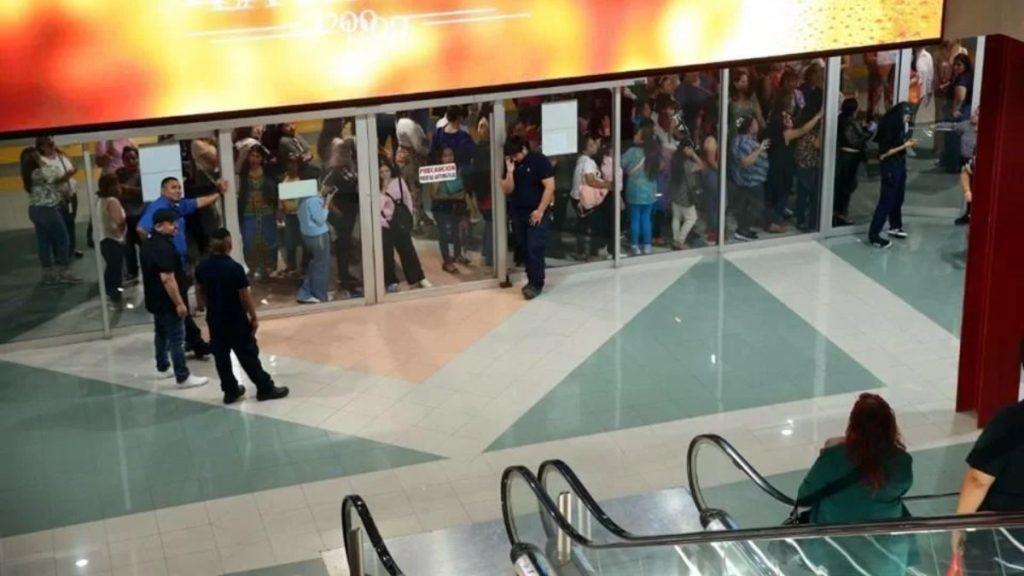Crowd of shoppers gathered behind glass doors at a mall entrance with security guards nearby.