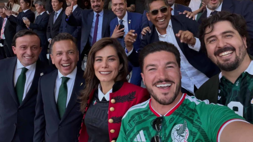 Group selfie of formally dressed attendees smiling and posing for a photo, with a man in a green Mexico jersey in the foreground taking the selfie.