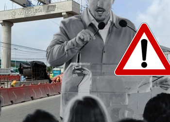 Speaker addressing a crowd at a road construction site with a large warning triangle overlay indicating caution.