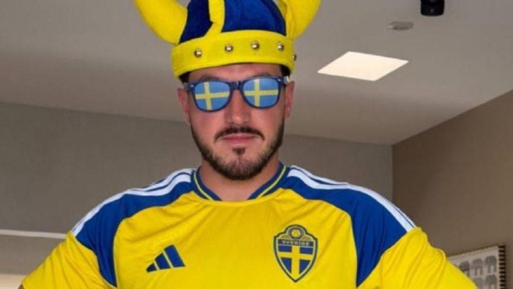 escandalo-en-el-juego-de-suecia-y-tunez - Minuto Cero Man in a Swedish soccer jersey wearing a yellow crown with blue horns and blue sunglasses reflecting the Swedish flag, posing indoors.