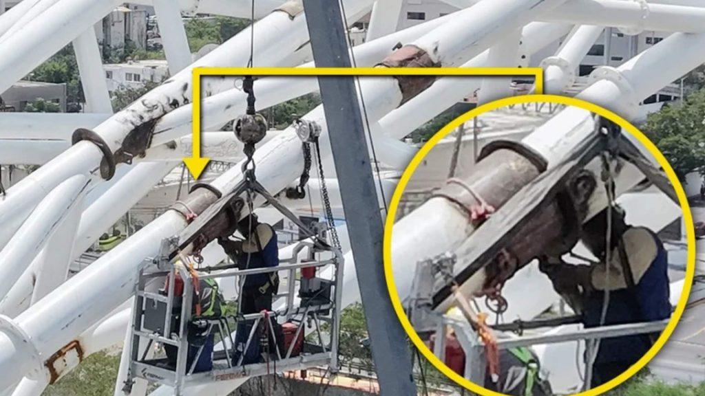 falla-puente-nuevo-rio-santa-catarina - Minuto Cero Workers in a suspended platform inspecting a large white steel framework, wearing safety harnesses and helmets.