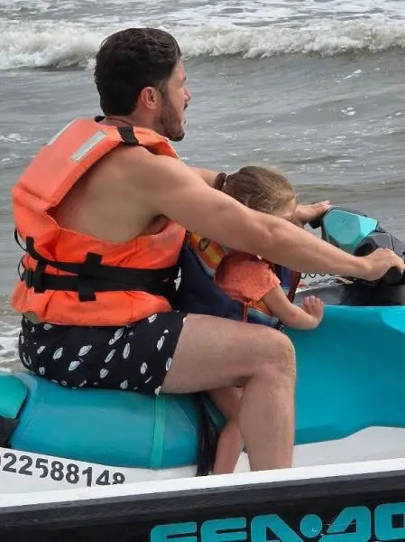 image - Minuto Cero Man with orange life jacket rides a jet ski, holding a child who wears a life jacket on a windy sea.