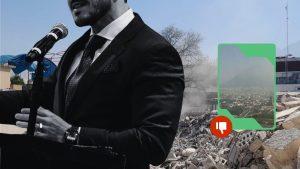 Man in a black suit speaks at a podium with a microphone, rubble behind him; an overlay shows a city view with a red thumbs-down badge indicating disapproval.