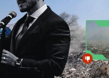 Man in a black suit speaks at a podium with a microphone, rubble behind him; an overlay shows a city view with a red thumbs-down badge indicating disapproval.